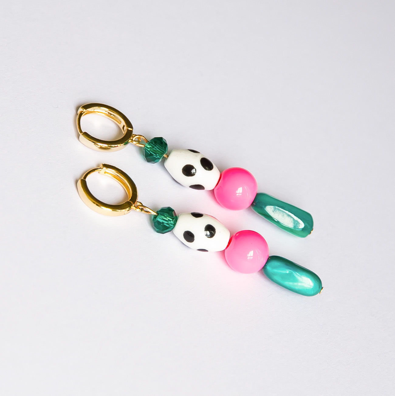 Pink and green bead earrings with a black and white dotted ceramic bead on a white background.