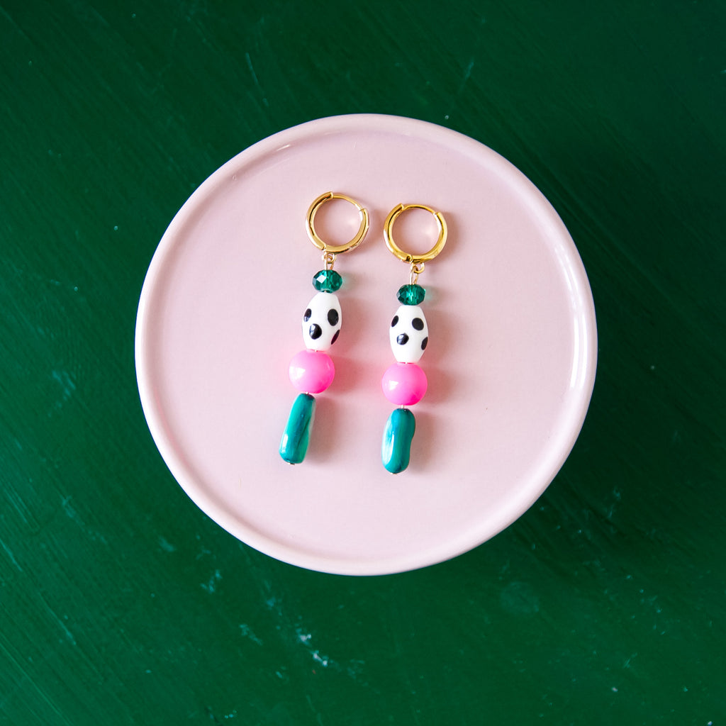 Pair of pink and green bead earrings on a pink plate with a green background