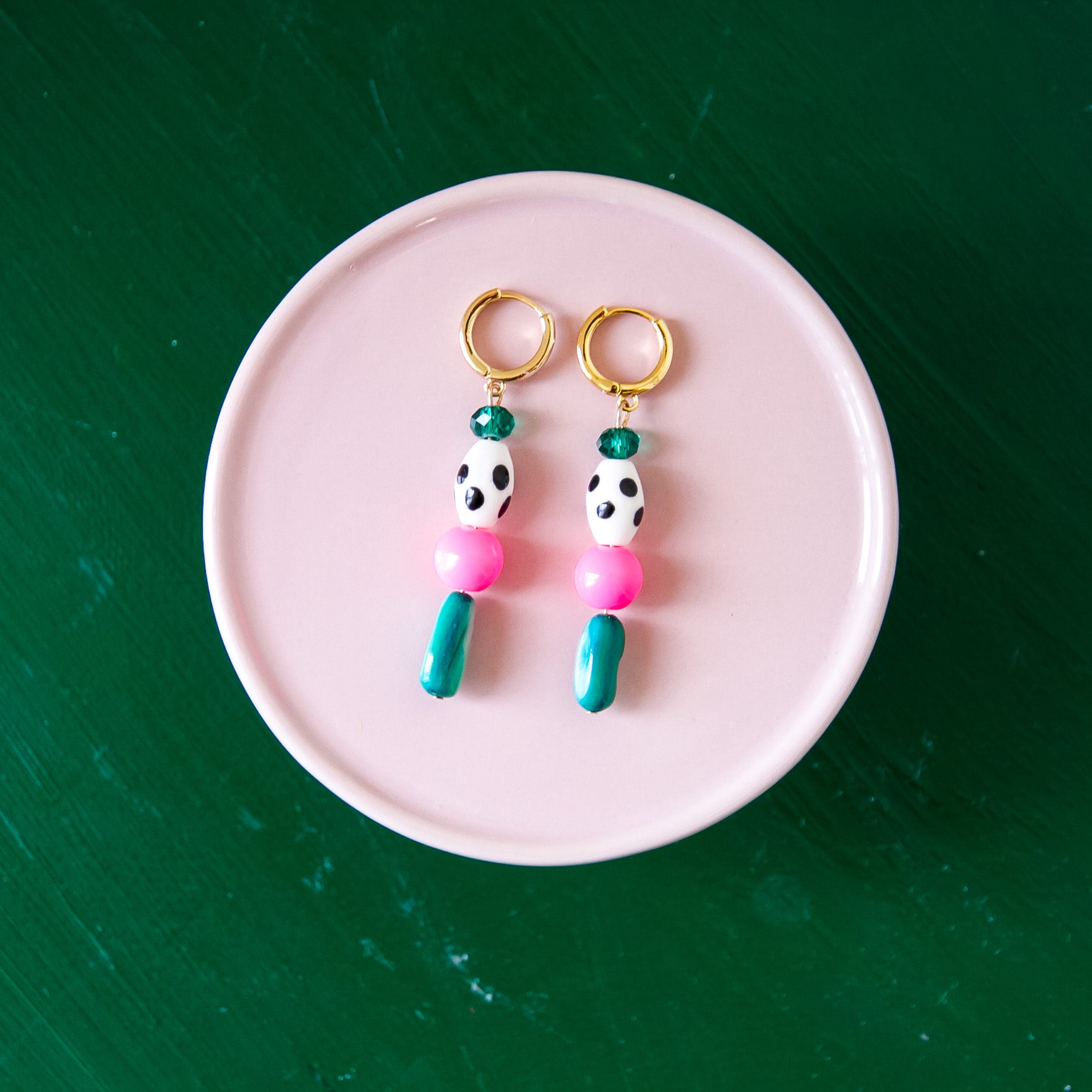 Pair of pink and green bead earrings on a pink plate with a green background